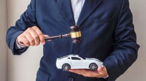 Pessoa de terno segurando martelo de leilão e miniatura de carro branco