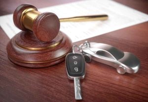 Martelo de leiloeiro ao lado de chave de carro e chaveiro em forma de automóvel sobre mesa de madeira
